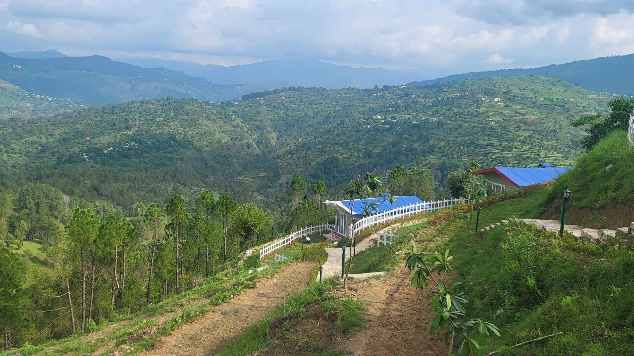 A view of a mountainous landscape with terraced fields, a white fence, and a building with a blue roof.