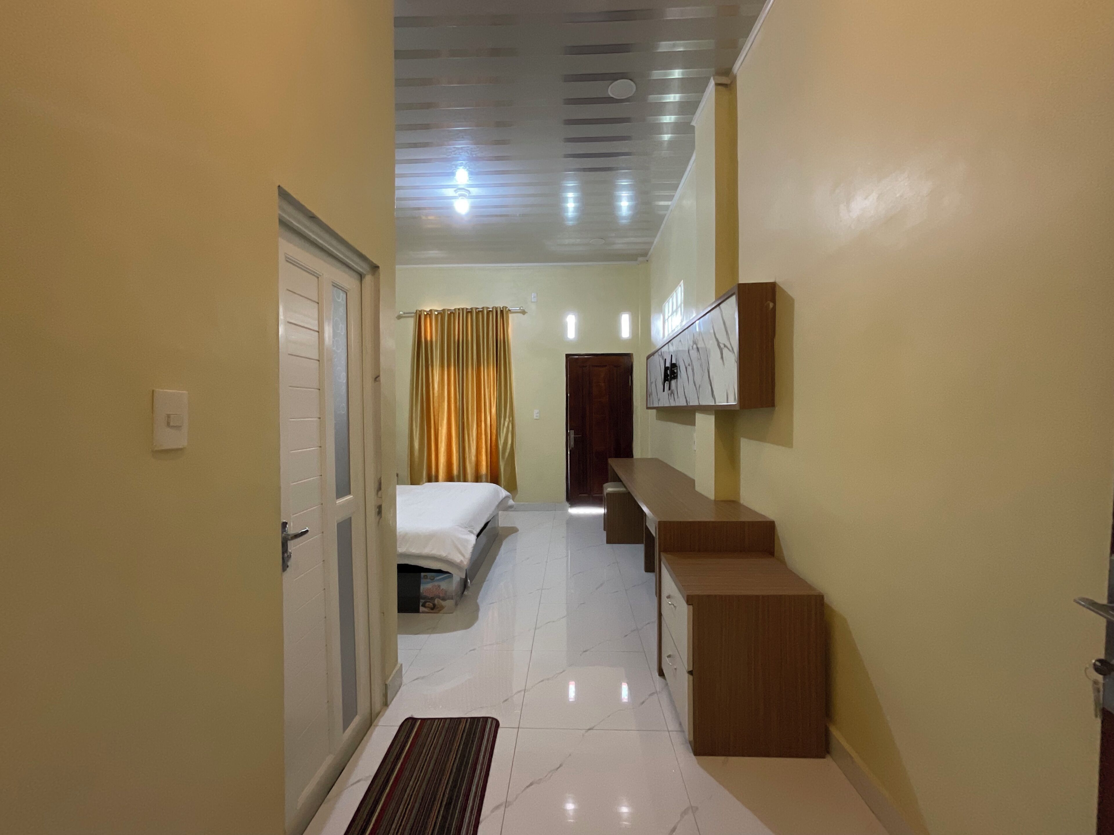 A hotel hallway with a bed, a bench, a TV mounted on the wall, and a door.