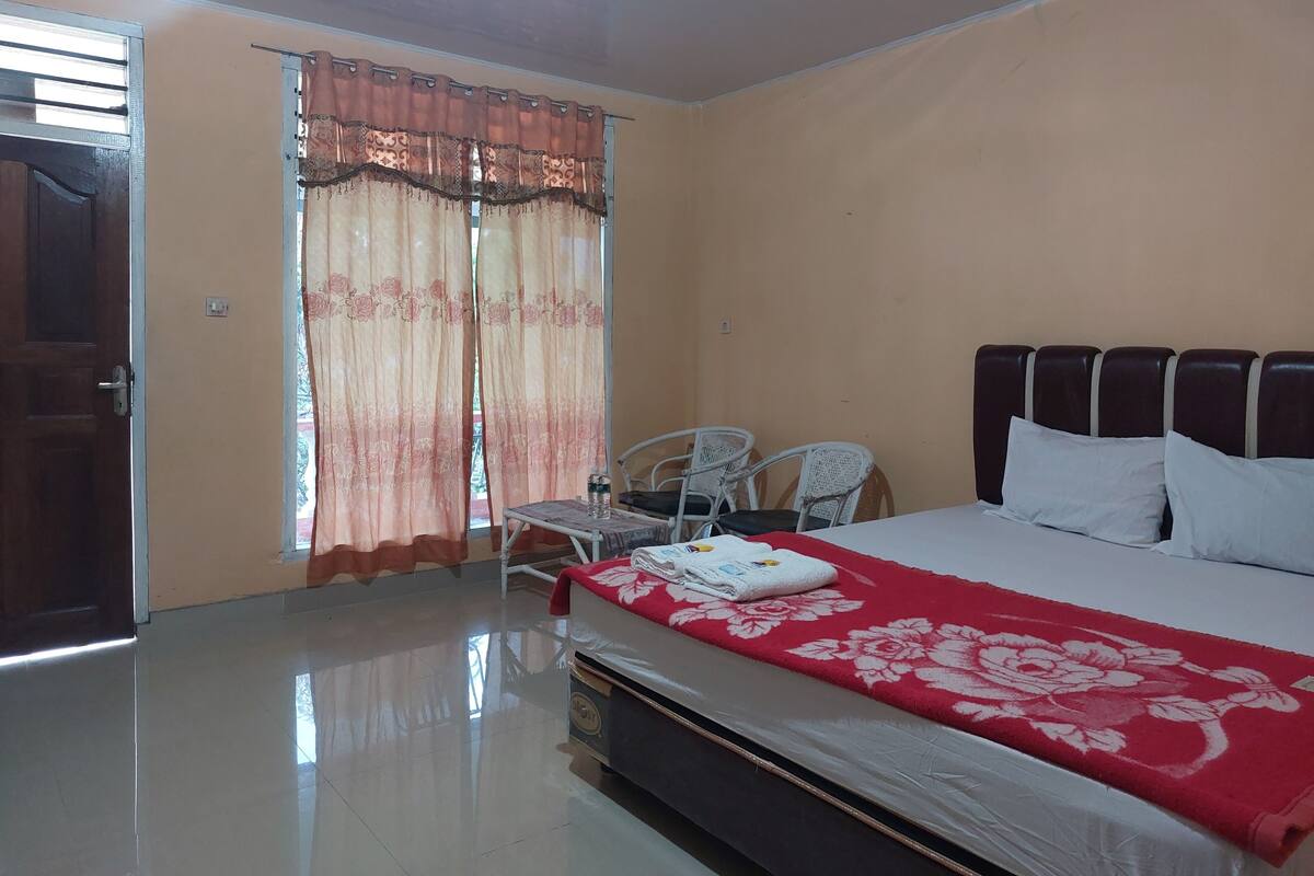 A hotel room with a bed, a chair, a table, and a window with curtains.