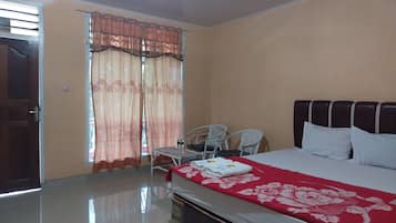 A hotel room with a bed, a chair, a table, and a window with curtains.