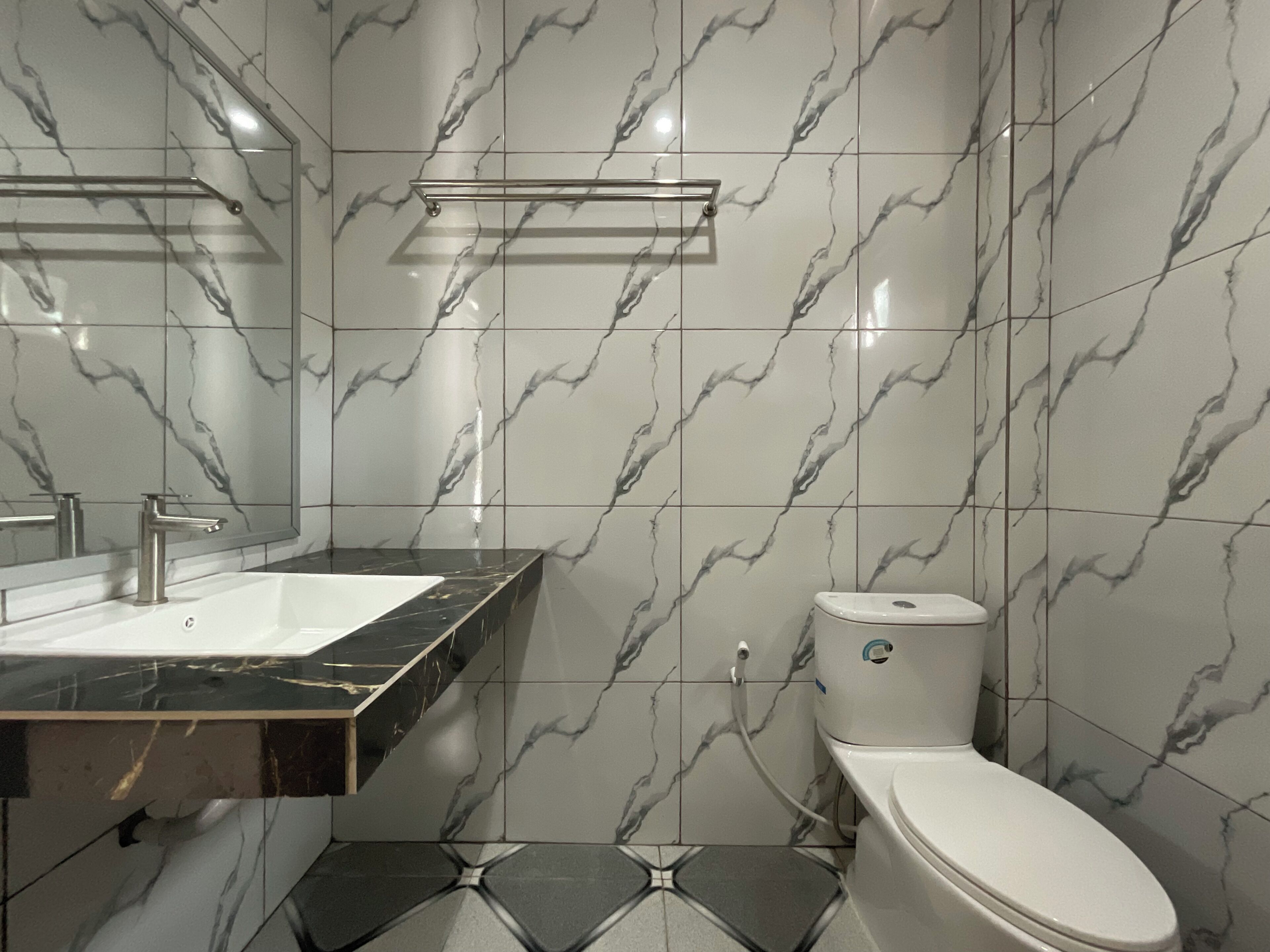 A bathroom with a white toilet, a sink with a black countertop, and marble-patterned walls.