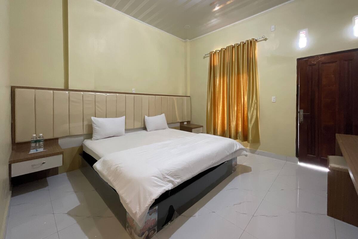 A hotel room with a large bed, a nightstand, a wooden door, and a curtain.