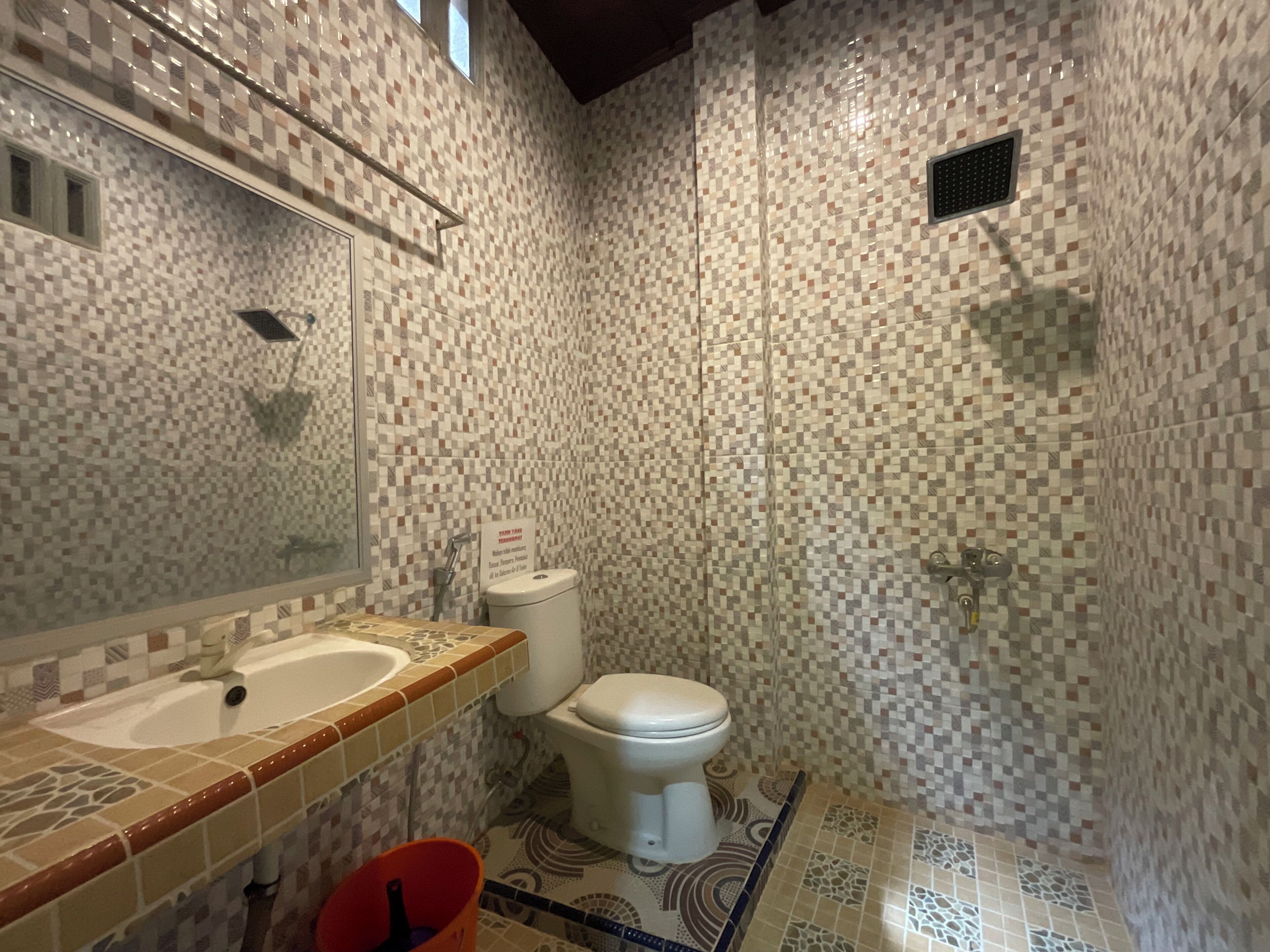 Une salle de bain avec un mur décoré d’une mosaïque de carreaux, un lavabo, des toilettes et un espace douche.