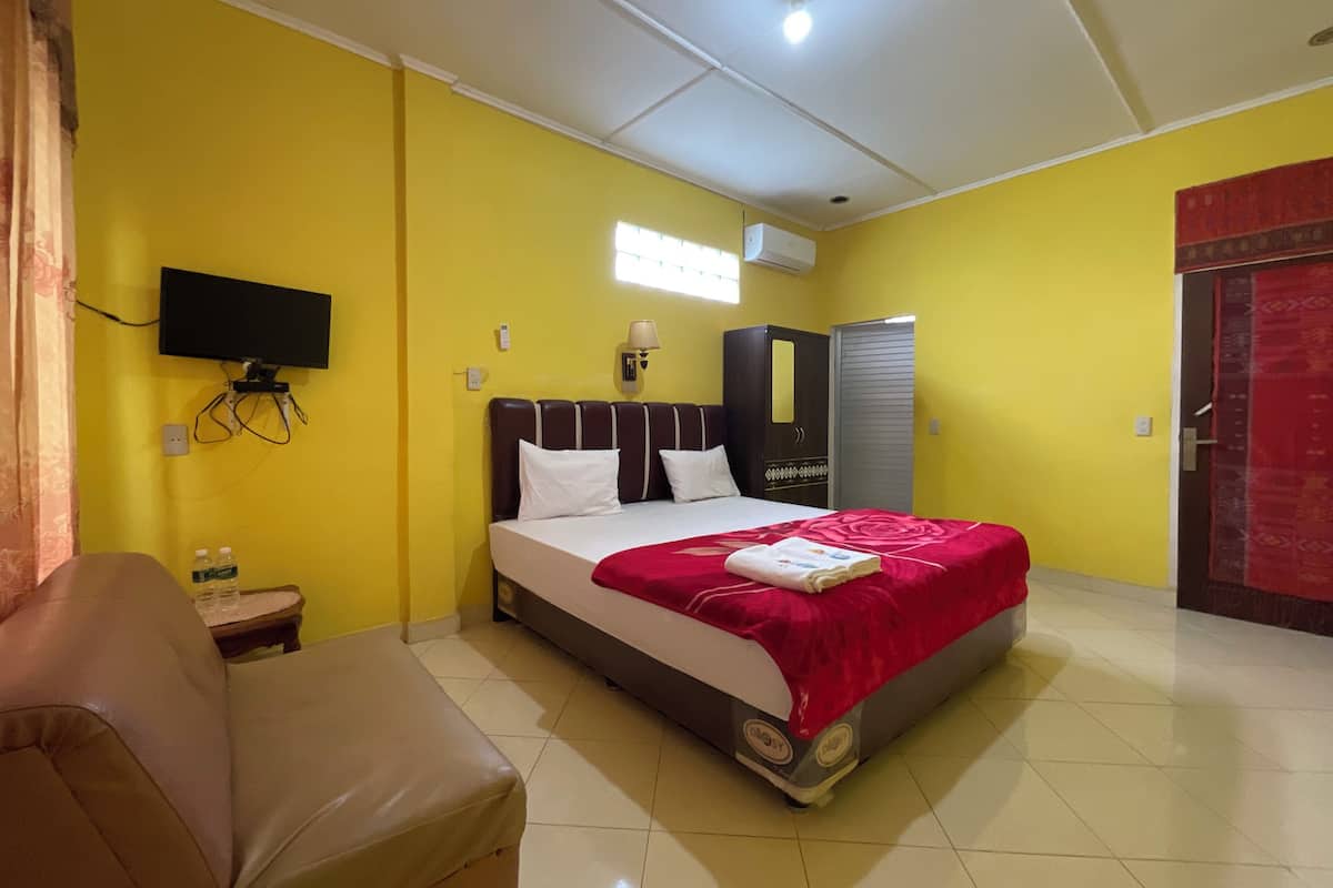 A hotel room with a bed, a TV mounted on the wall, a wardrobe, and a red door.