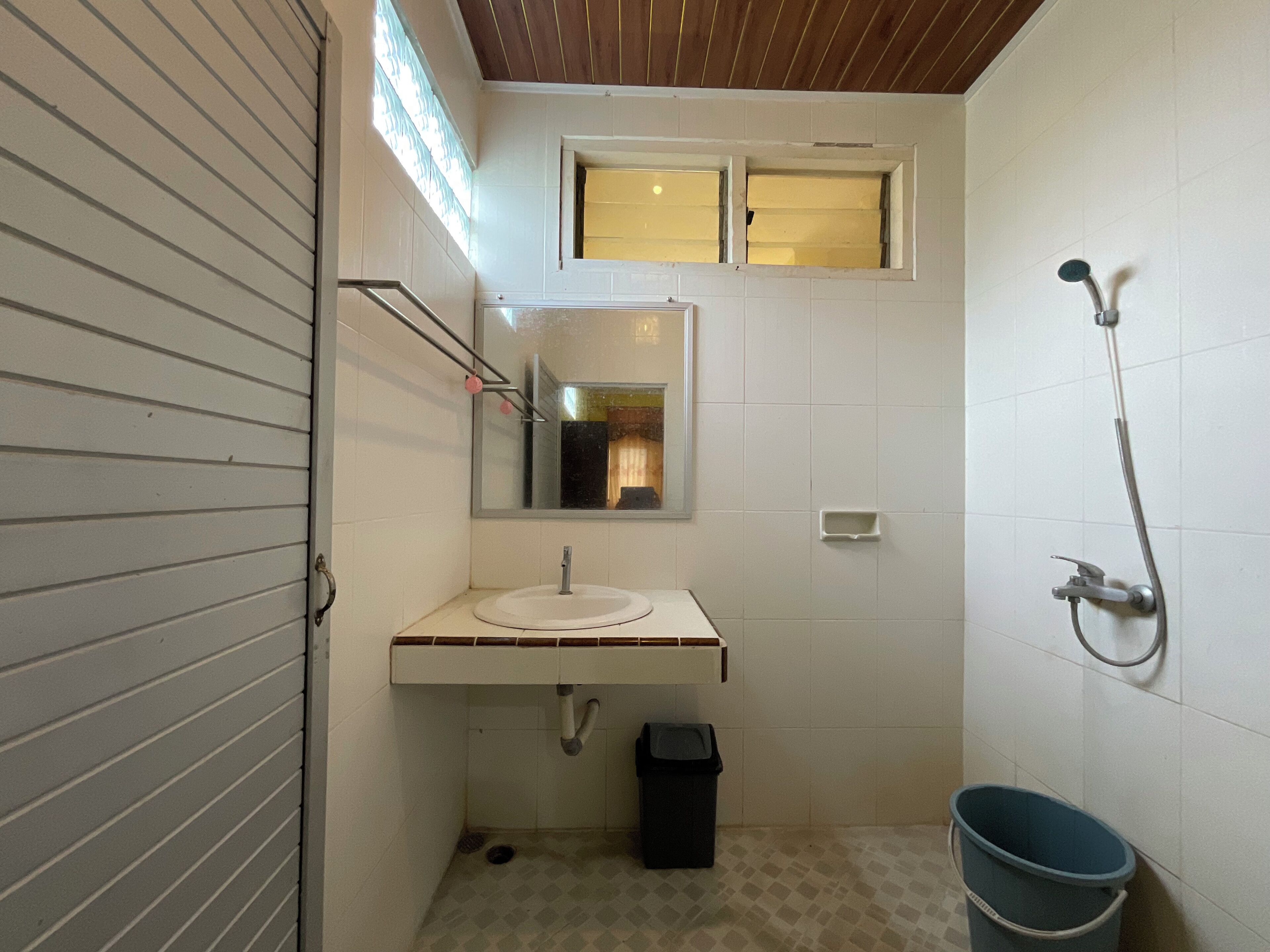 A small bathroom with a sink, mirror, shower, and a window.