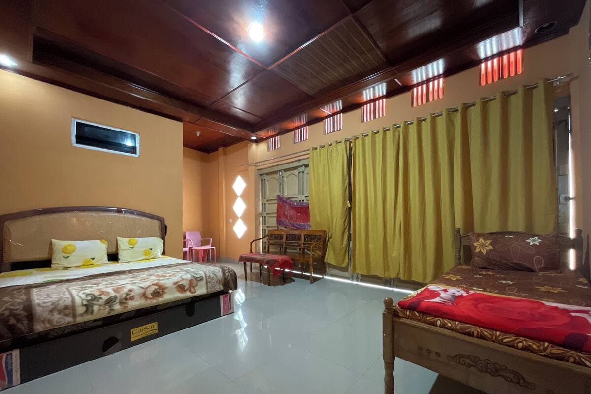 A hotel room with two beds, a small table, a chair, and a window with curtains.