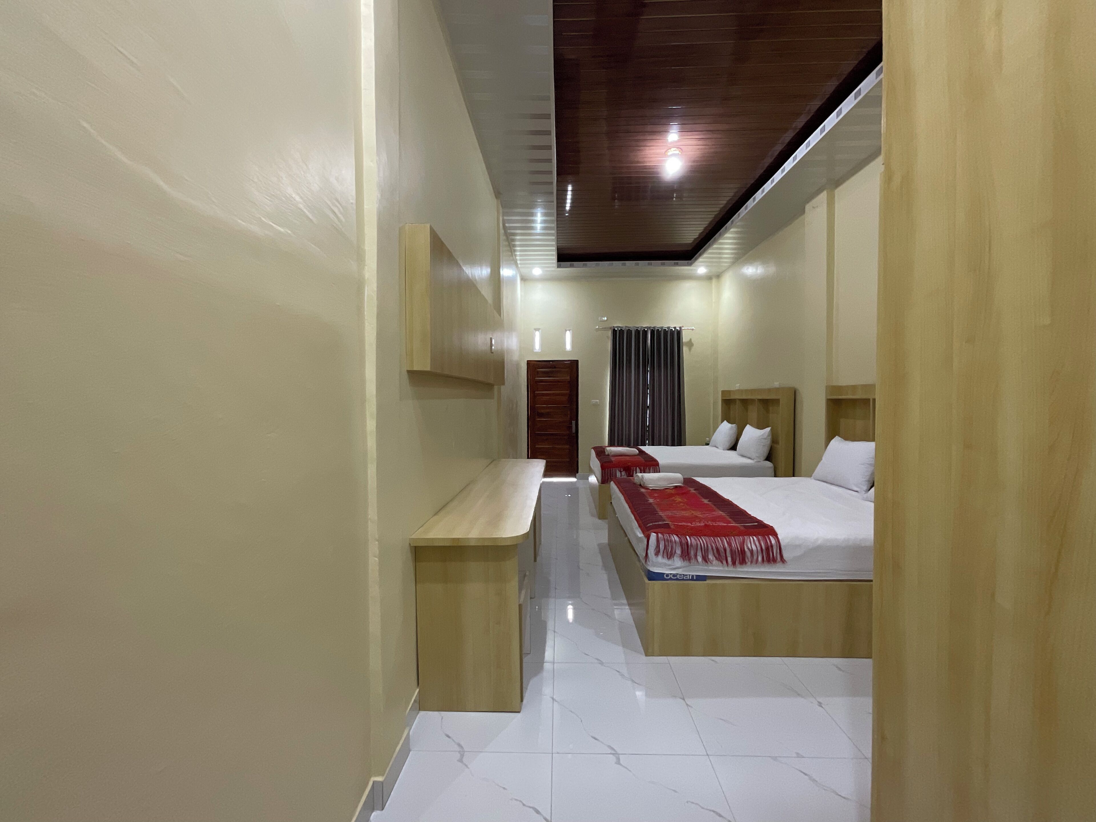 Habitación de hotel con dos camas, un banco de madera, un escritorio y una lámpara en el techo.