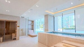 A modern spa room with a wooden sauna, a glass shower enclosure, and a large window offering a city view. - Binghatti Royale Residences - JVC (Dubai)