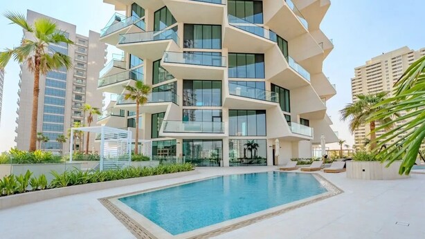 A modern building with a pool, surrounded by palm trees and other greenery. - Binghatti Royale Residences - JVC (Dubai)