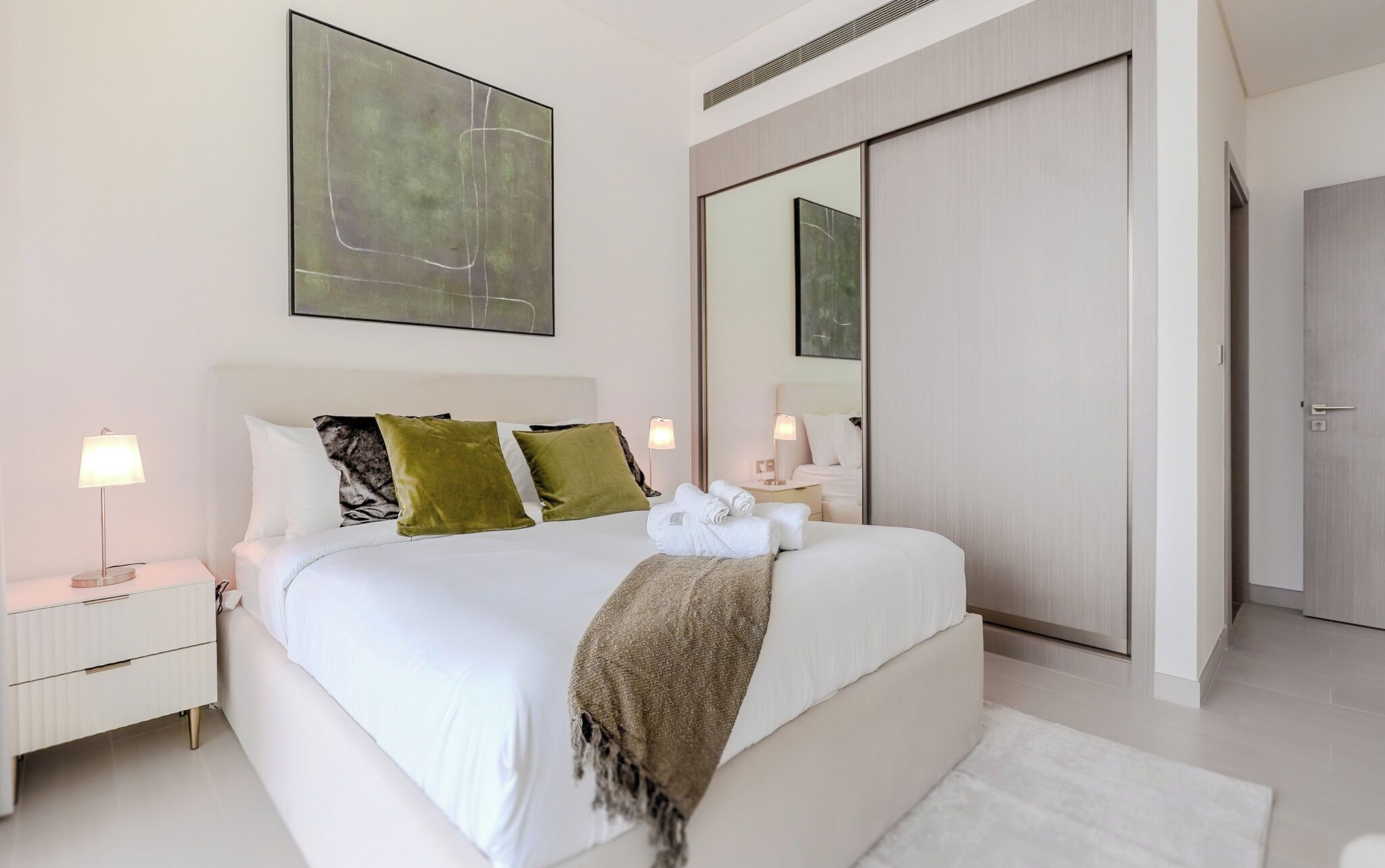 Une chambre d’hôtel moderne avec un grand lit, une table de chevet, une lampe de chevet, un miroir et une armoire.