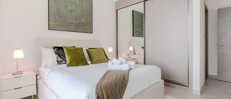 Une chambre d’hôtel moderne avec un grand lit, une table de chevet, une lampe de chevet, un miroir et une armoire.