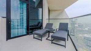 A balcony with two grey lounge chairs and a small table, overlooking a cityscape. - Binghatti Royale Residences - JVC (Dubai)