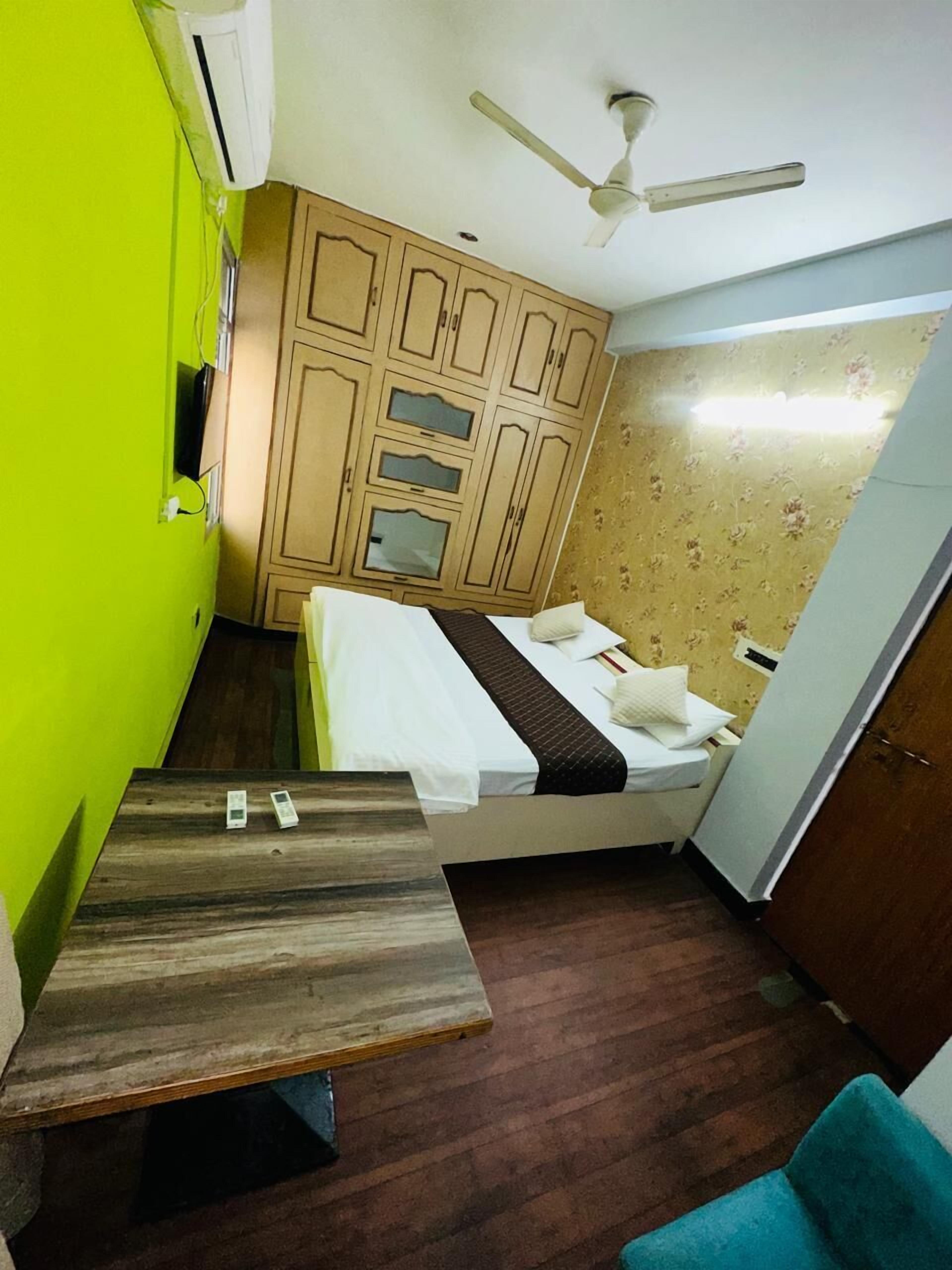 A compact room with a bed, a small table, a ceiling fan, and a wardrobe.
