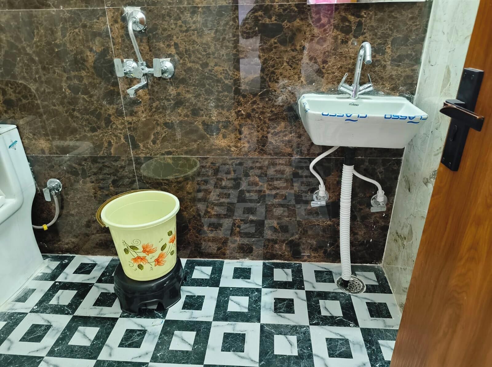 Ein Badezimmer mit Marmorboden, einem Waschbecken, einer Toilette und einem Eimer.