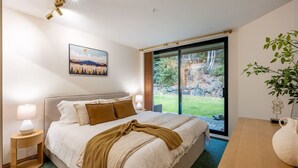 Ein Schlafzimmer mit Bett, Nachttischlampen, einem Fenster mit Blick auf einen Wald und einem Gemälde an der Wand.