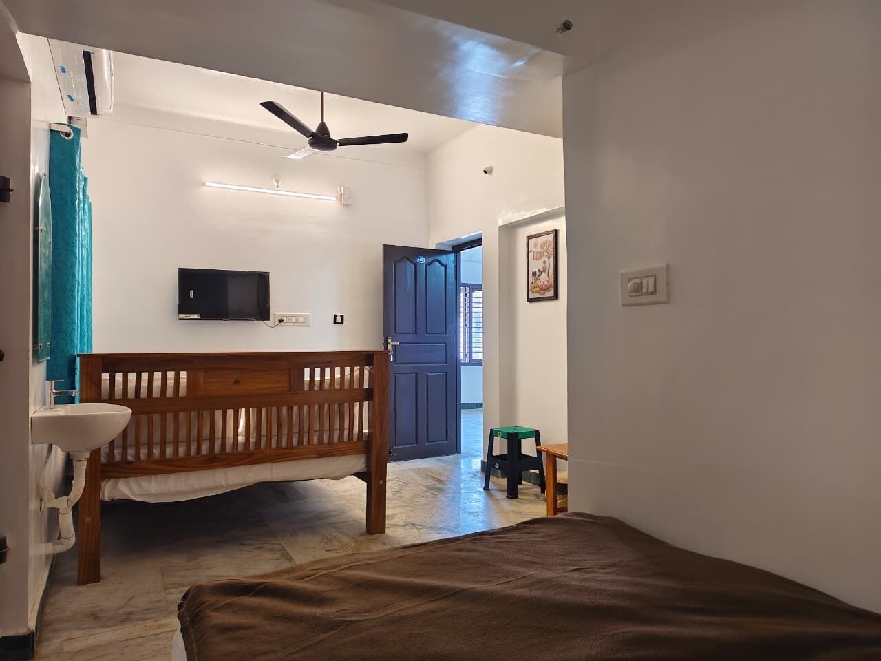 A room with a bed, a wooden bench, a small stool, a television, and a door leading to another room.