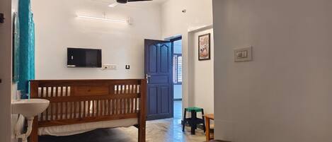 A room with a bed, a wooden bench, a small stool, a television, and a door leading to another room.