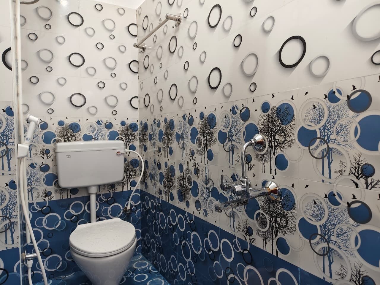 Une salle de bain comprenant des toilettes, une douche et un lavabo. Les murs sont décorés de motifs circulaires et de dessins d’arbres.
