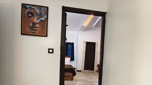 A hallway leading to a bedroom with a bed, a door, and a painting on the wall. - Sri Inn (Puducherry)