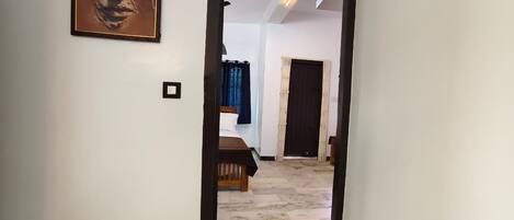 A hallway leading to a bedroom with a bed, a door, and a painting on the wall.