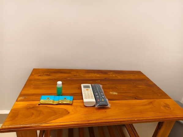 A wooden table with a remote control, a bottle, and a packet of tissues. - Sri Inn (Puducherry)