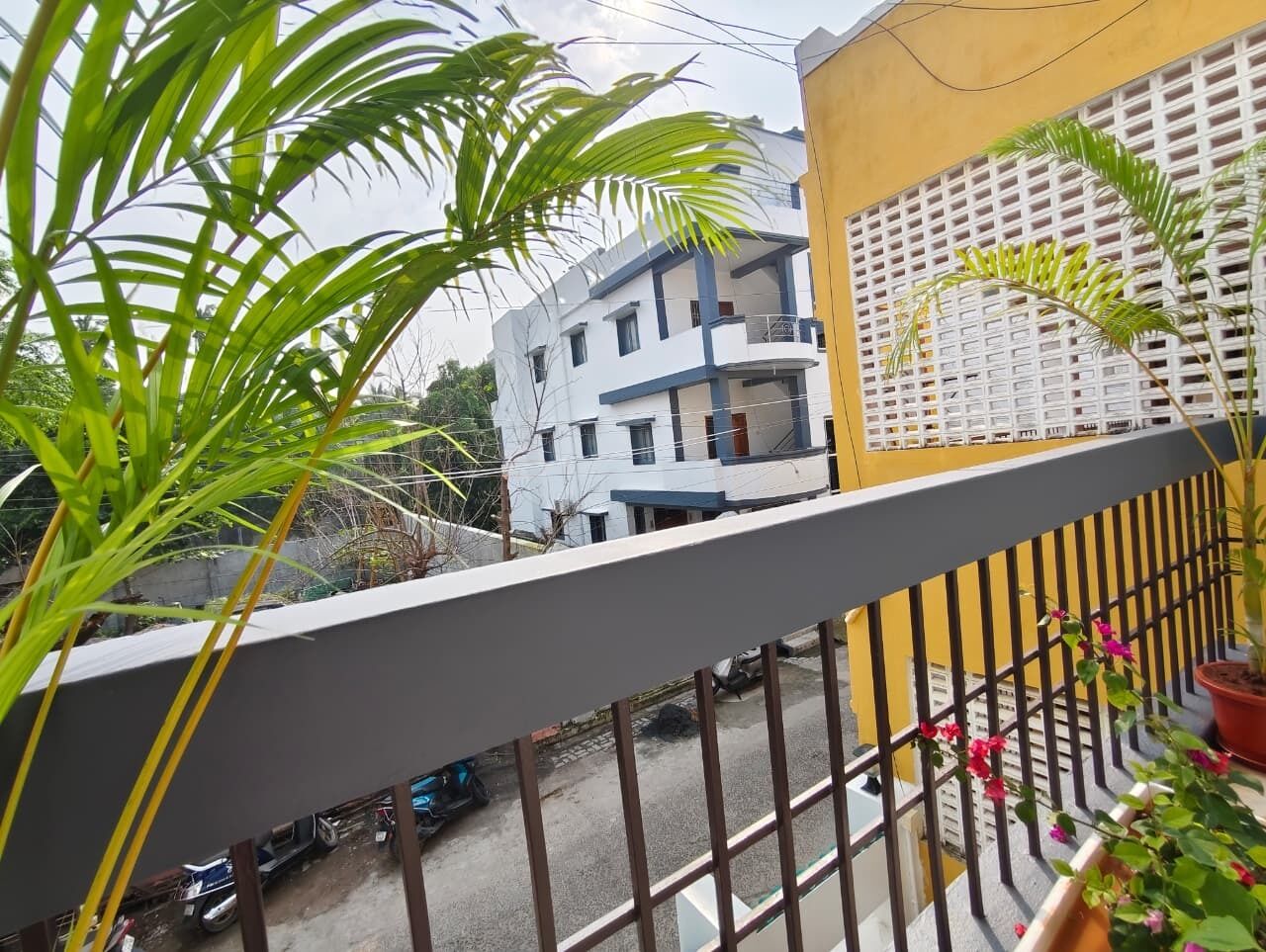 A balcony with a metal railing, a potted plant, and a view of a multi-story building with balconies.