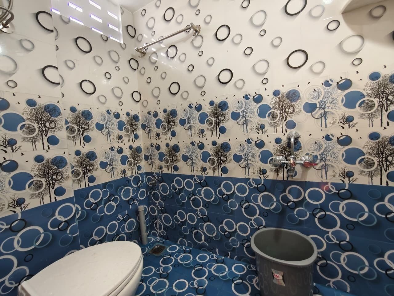A bathroom with a blue and white circular pattern on the walls and floor, a white toilet, and a shower area.