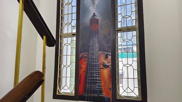 A staircase with a wooden handrail and a stained glass window depicting a train. - Sri Inn (Puducherry)