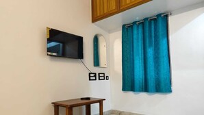 A room with a wooden table, a mounted TV, a blue curtain, and a mirror. - Sri Inn (Puducherry)