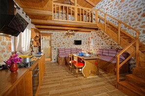 A rustic kitchen with wooden cabinets, a dining area with a bench, and a stone wall. - Sea Front Kallia & George Villa, By IdealStay (7FV9+QRC Malia, Greece)