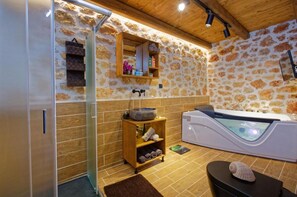 A spa room with a stone wall, wooden shelves, a stone basin, a massage table, and a hot tub. - Sea Front Kallia & George Villa, By IdealStay (7FV9+QRC Malia, Greece)