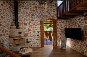 A stone-walled room with a fireplace, a television mounted on the wall, and a wooden staircase. - Seafront Villa Kallia & George, Villa (7FV9+QRC Malia, Greece)