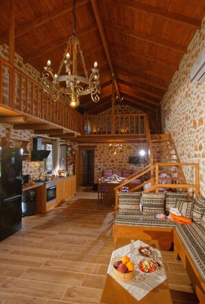 A spacious loft with a high ceiling, exposed wooden beams, a stone wall, and a cozy seating area with patterned cushions. - Sea Front Kallia & George Villa, By IdealStay (7FV9+QRC Malia, Greece)