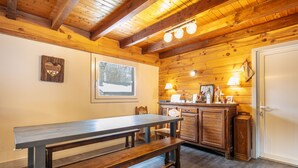 Un interior de madera con una larga mesa de comedor, bancos, una zona de cocina y una puerta blanca.