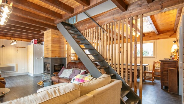 Un interior de madera con una escalera, un sofá, una chimenea y un comedor.