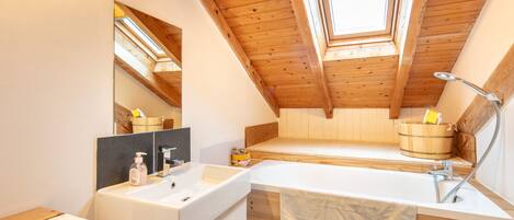A modern bathroom with a skylight, wooden beams, a bathtub, and a vanity with a mirror.