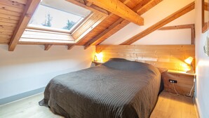 Un dormitorio con techo inclinado, tragaluz, cama, lámparas de noche y cabecera de madera.