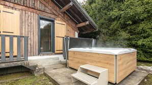 Una cabaña de madera con jacuzzi y una pequeña terraza de madera.
