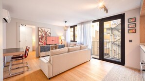 Un soggiorno moderno con un divano, un'area pranzo con tavolo e sedie, una TV e un balcone con vista sulla città.