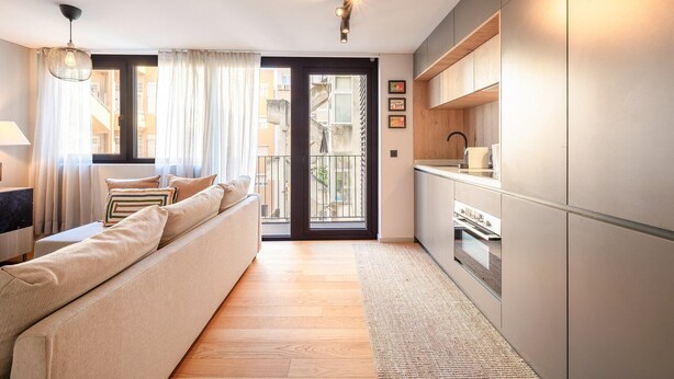 Un appartamento moderno con un divano, angolo cottura e vista attraverso una porta vetrata.