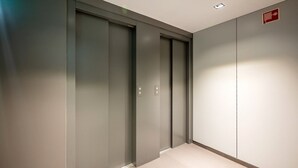 Un corridoio con due porte chiuse, un rilevatore di fumo a parete e un lampadario al soffitto.