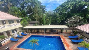 Piscina con sillas de descanso, rodeada de plantas en macetas y un área de estar techada.