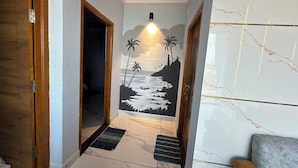 A hallway with a wooden door, a dark rug, a wall mural of a beach scene, and a marble floor. - Arna Inn Luxury Stay (Bhatkal)