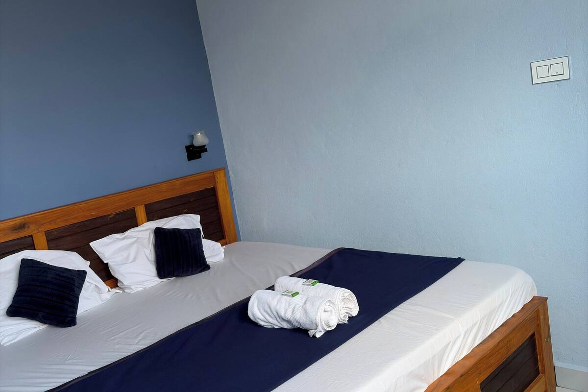 A neatly made bed with a wooden headboard, white linens, and a dark blue bedspread.