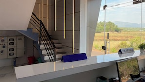 A modern interior with a staircase, a reception desk, and a view of a rural landscape. - Arna Inn Luxury Stay (Bhatkal)