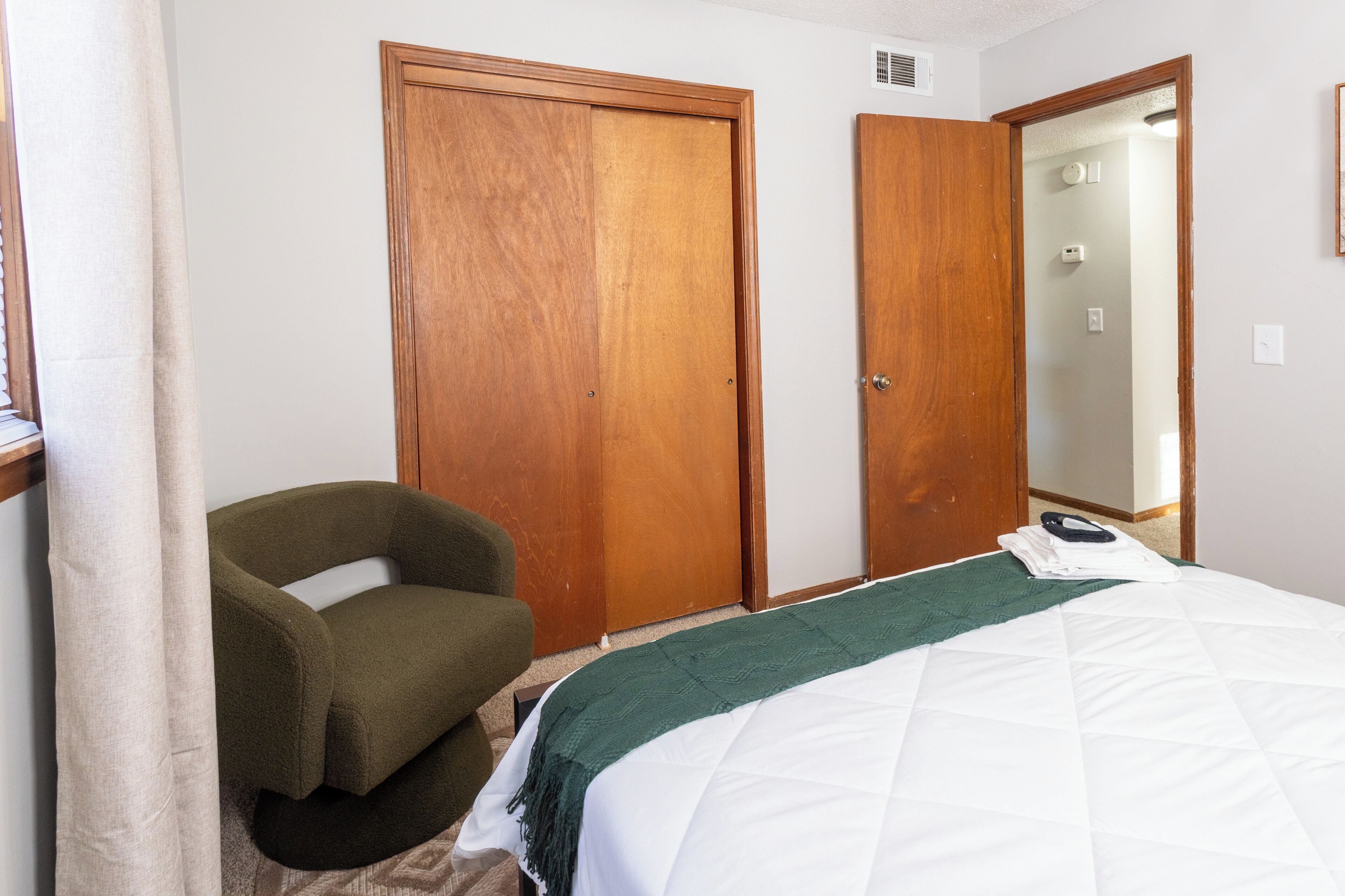 A hotel room with a bed, a green armchair, and two wooden doors.