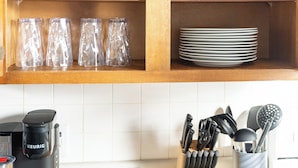 A kitchen with wooden shelves holding glassware and plates, a coffee maker, and a knife block. - Near K-State Campus - Central Manhattan Stay (Manhattan)