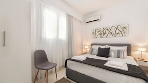 Ett modernt hotellrum med en stor säng, en stol, en väggmonterad luftkonditioneringsanläggning och en tavla med ett bambumotiv.