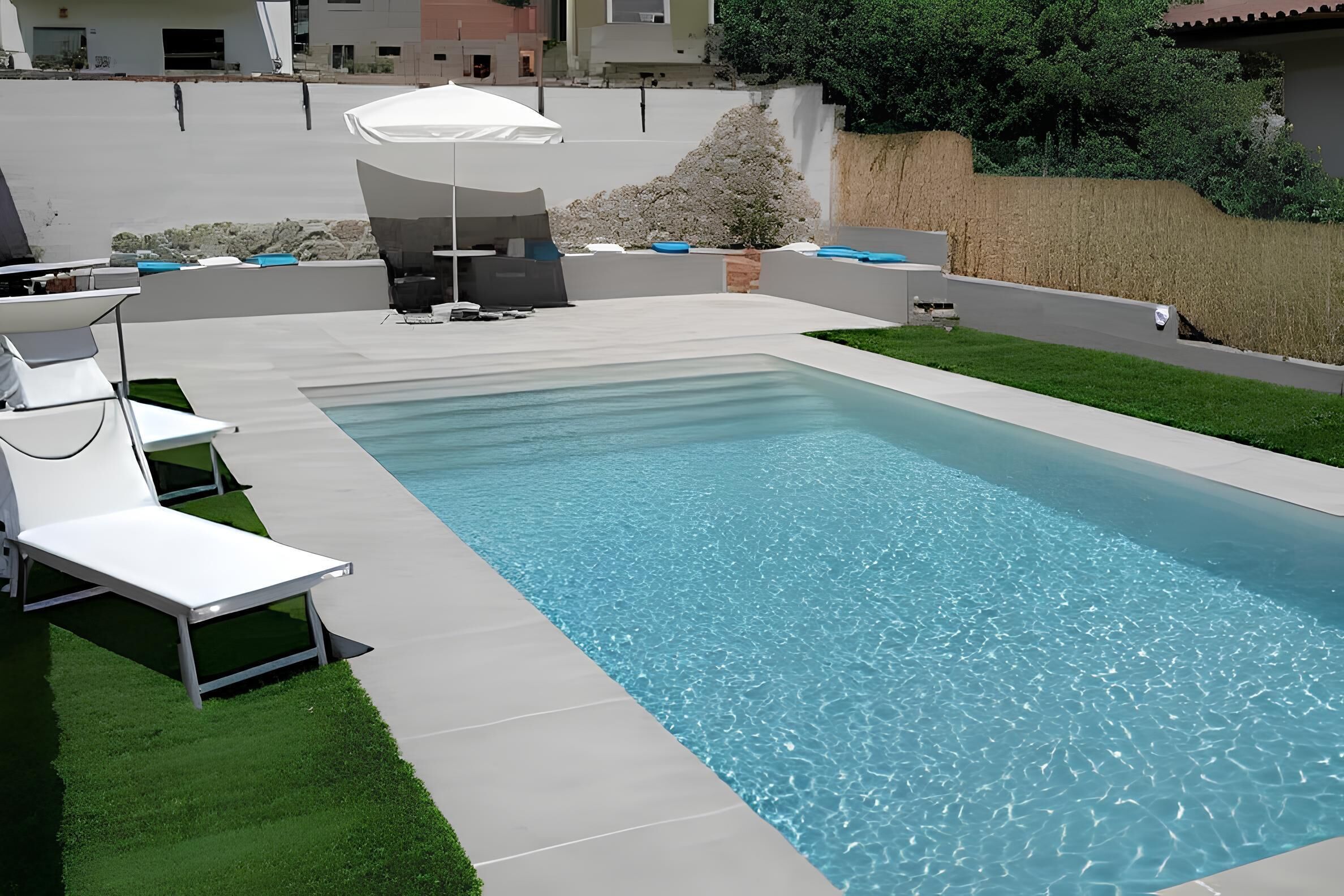 Een rechthoekig zwembad met helderblauw water, omringd door een geplaveid terras. Er staan witte ligbedden en een witte parasol voor schaduw.