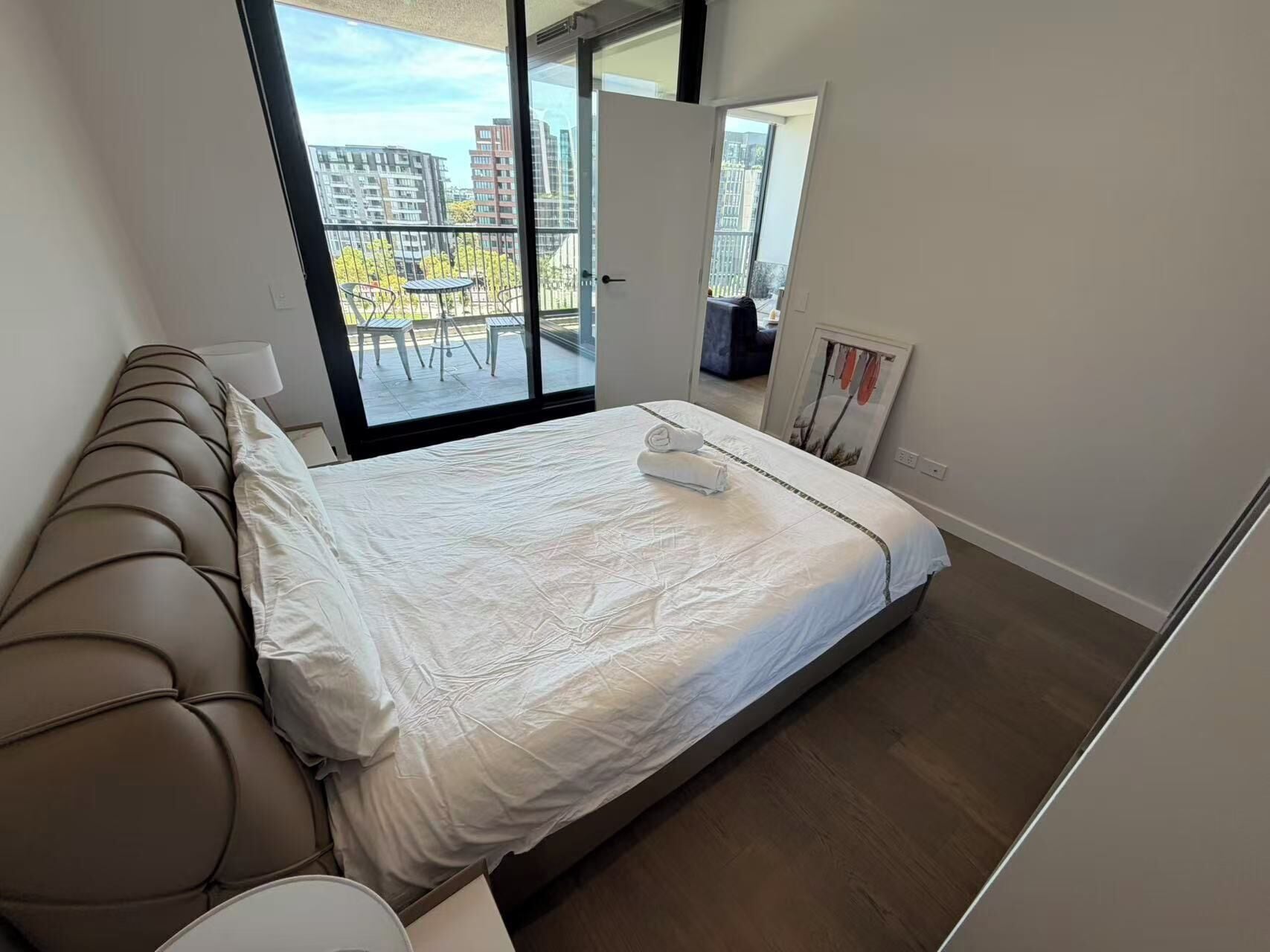 A modern bedroom with a large bed, a sofa, and a balcony with a view of buildings.